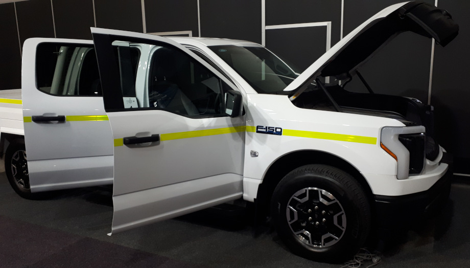 White F150 Lightning with lime reflective tape and all 4 doors and the front trunk open.